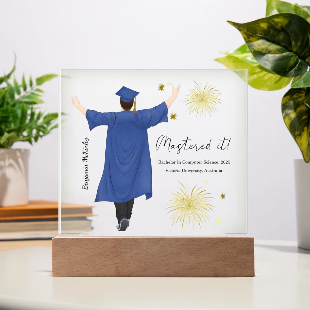 Graduation-themed decorative plaque with a person in a blue gown and cap, 'Mastered it!' text, and fireworks design on a wooden stand.